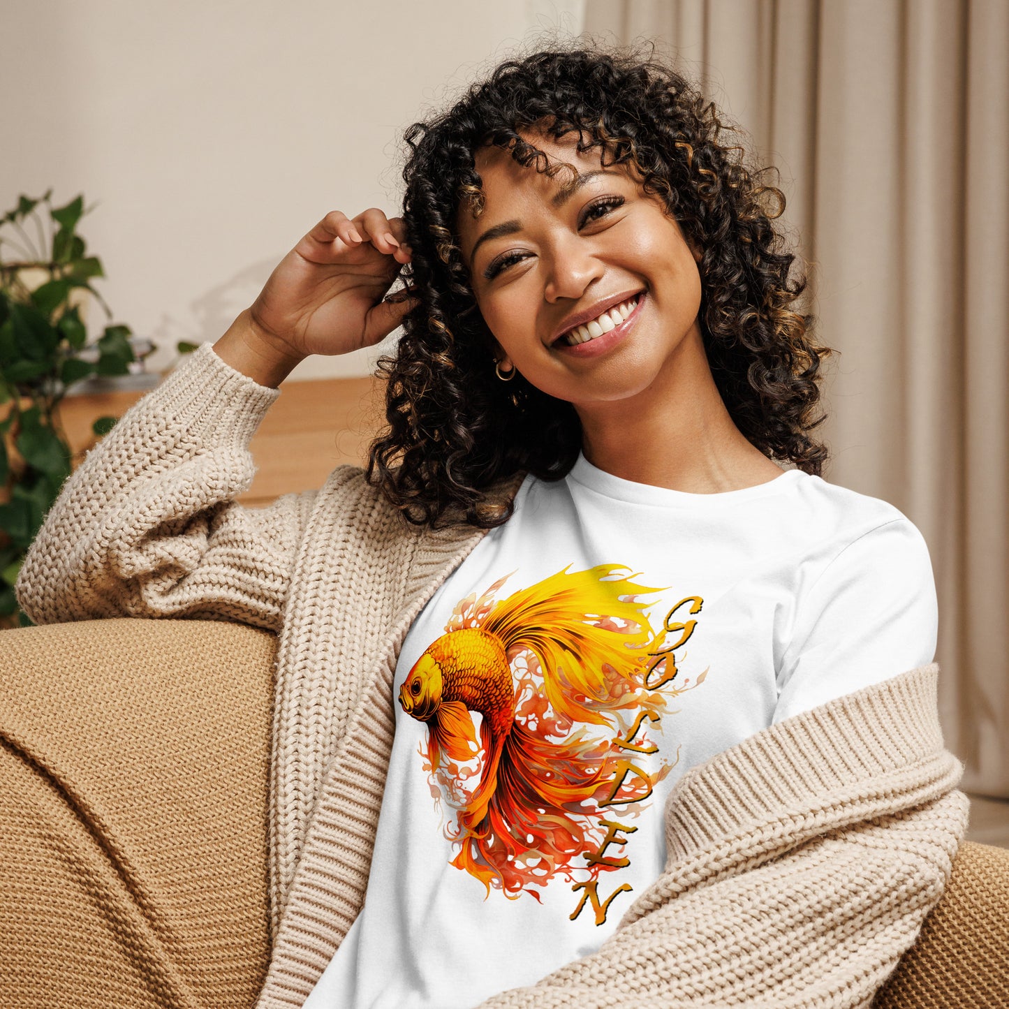Model draagt wit relaxed fit T-shirt met grote gouden goldfish illustratie: zittend op de bankstel, focus op levendige oranje en goud kleurenprint.voor aanzicht
