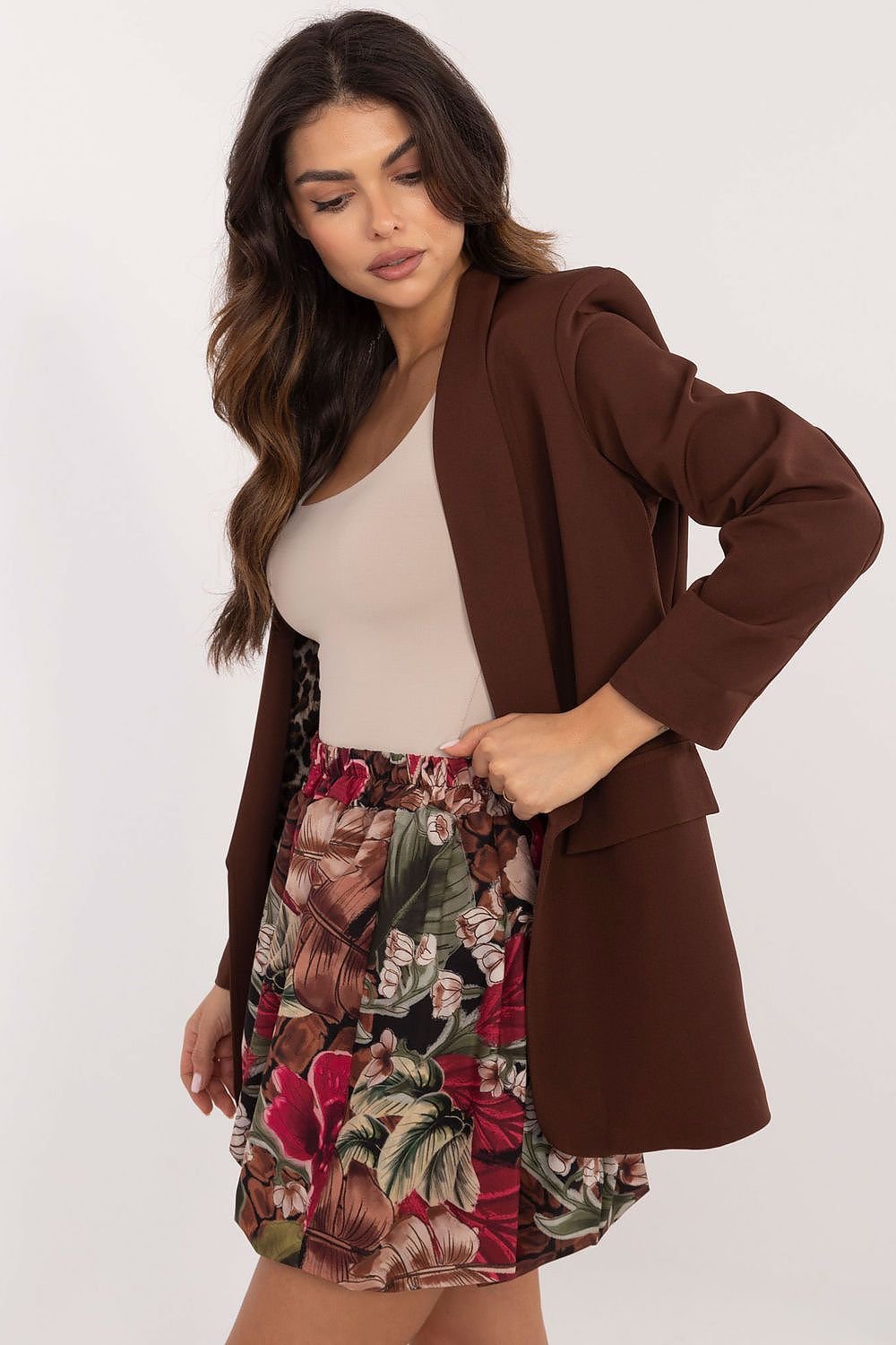 Een vrouw draagt een stijlvolle minirok met bomber snit en bloemenprint, perfect voor een casual zomerlook, beige  t-shirt met een bruine blazer, beige achtergrond,