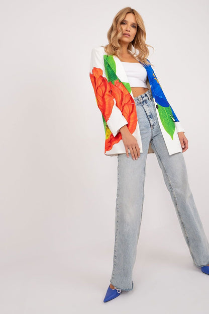 Vrouw draagt een witte blazer met grote, kleurrijke bloemenprint, gecombineerd met een witte crop top en jeans. Witte achtergrond