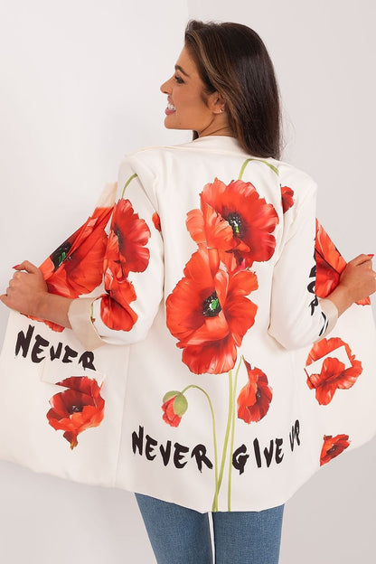 Vrouw draagt een witte blazer met rode bloemenprint en zwarte tekst details, gecombineerd met een beige top, achter zijde