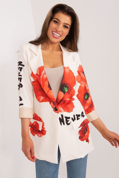 Blije Vrouw draagt een witte blazer met rode bloemenprint en zwarte tekst details, gecombineerd met een beige top. Een jeans broek, voorzicht