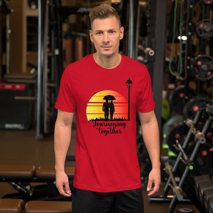 Een unisex rood T-shirt met de titel 'Journeying Together', afbeelding van een koppel hand in hand, gedragen door een man, met een sportschoolachtergrond, vooruitkijkend.